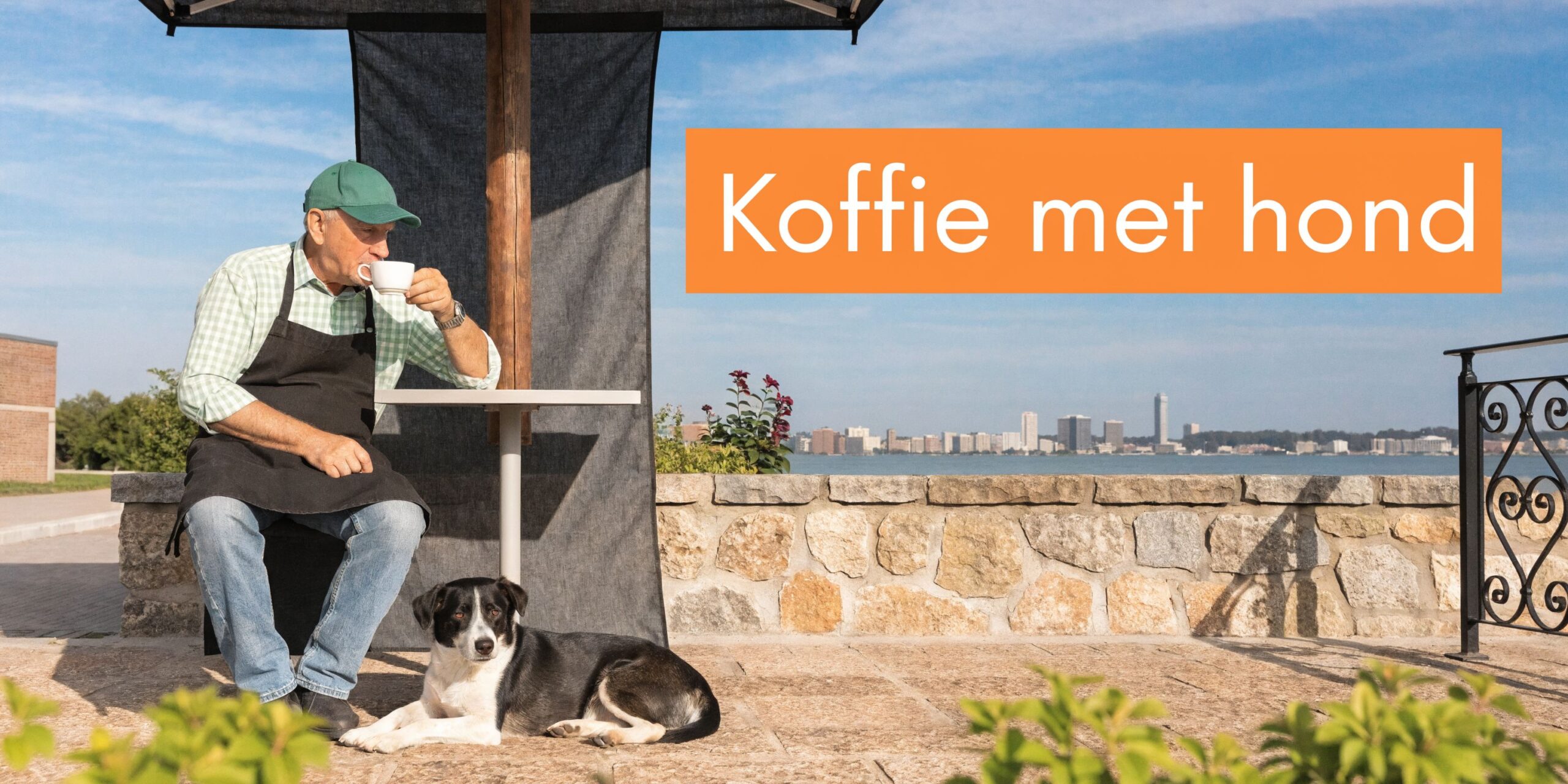 Een oudere man met een schort drinkt koffie aan een tafel buiten met zijn hond